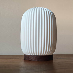 Lampara de mesa modelo Aura color Blanca encendida, con base en madera de Nogal natural.